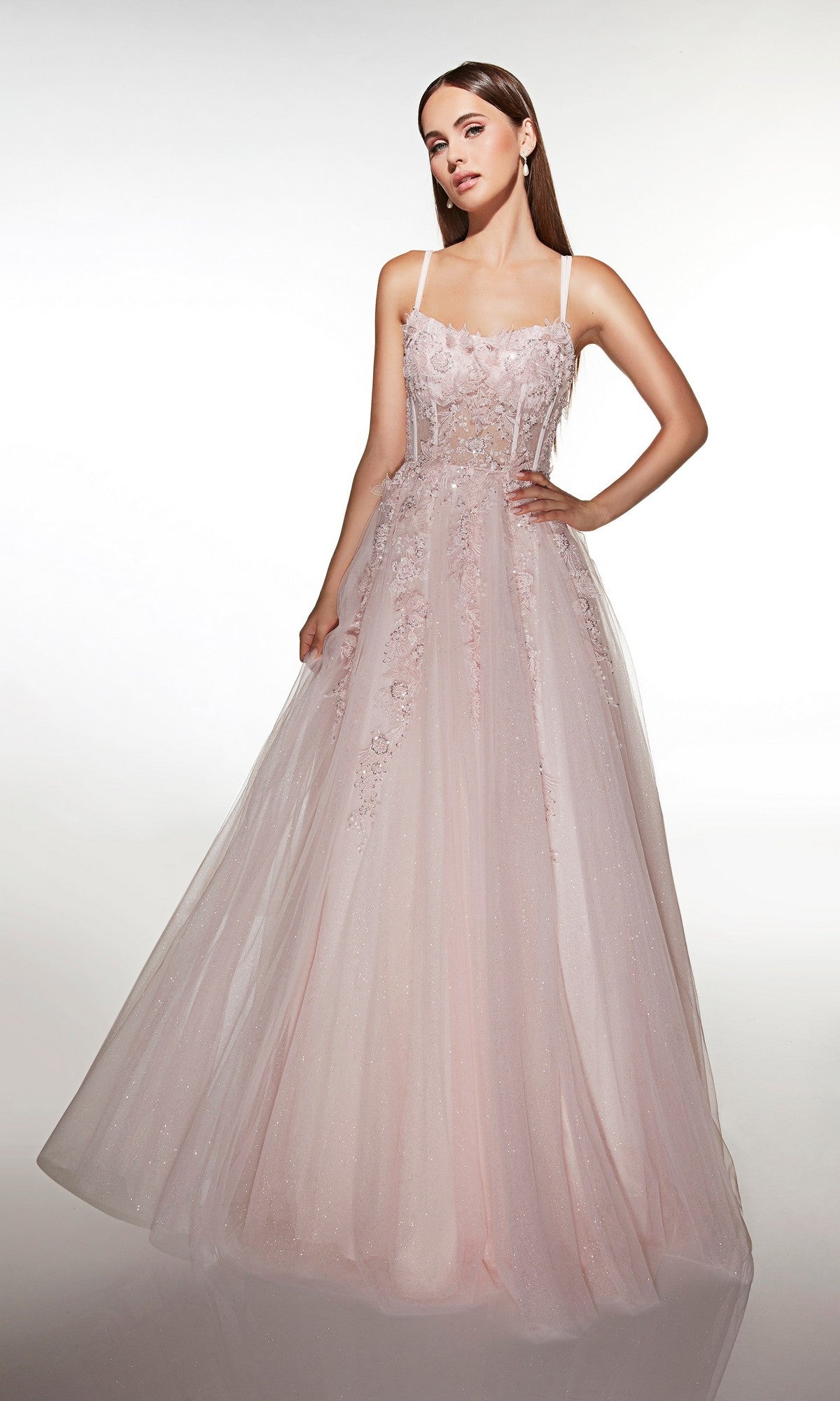 A woman models the Alyce 62203 Long Prom Dress, featuring a light pink hue, corset bodice, sheer overlay, and delicate 3D floral appliqués against a white background.